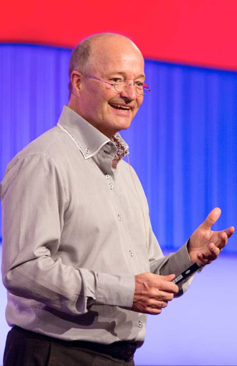 Gregor Staub bei einem Vortrag, Mikrofon am Ohr, eine Hand erhoben